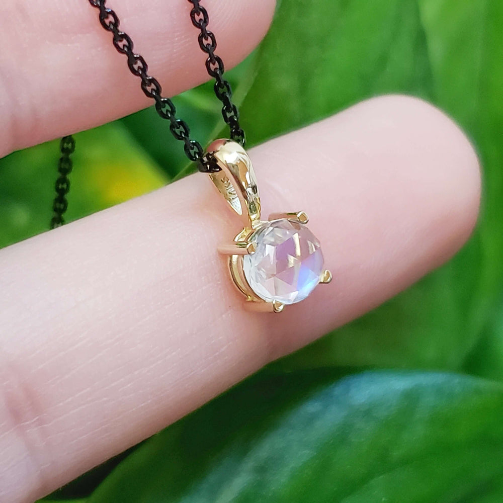14kt yellow gold rose cut moonstone pendant on a black chain, shown on a fingertip