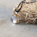 Close-up of 14kt yellow gold rose cut moonstone pendant on a black chain beside natural material