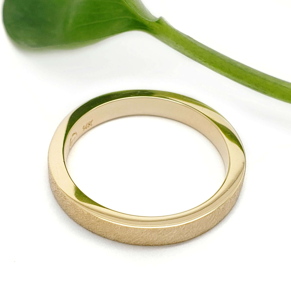 14kt yellow gold saw blade textured wedding ring by Era Design, shown beside a green leaf