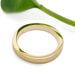 14kt yellow gold saw blade textured wedding ring by Era Design, shown beside a green leaf