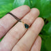 14kt yellow gold shield-cut green sapphire pendant on a black chain, shown on a hand with green background