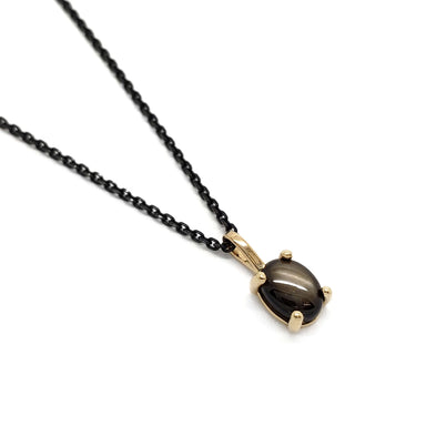 14kt yellow gold pendant with oval black star sapphire on a black chain, angled view