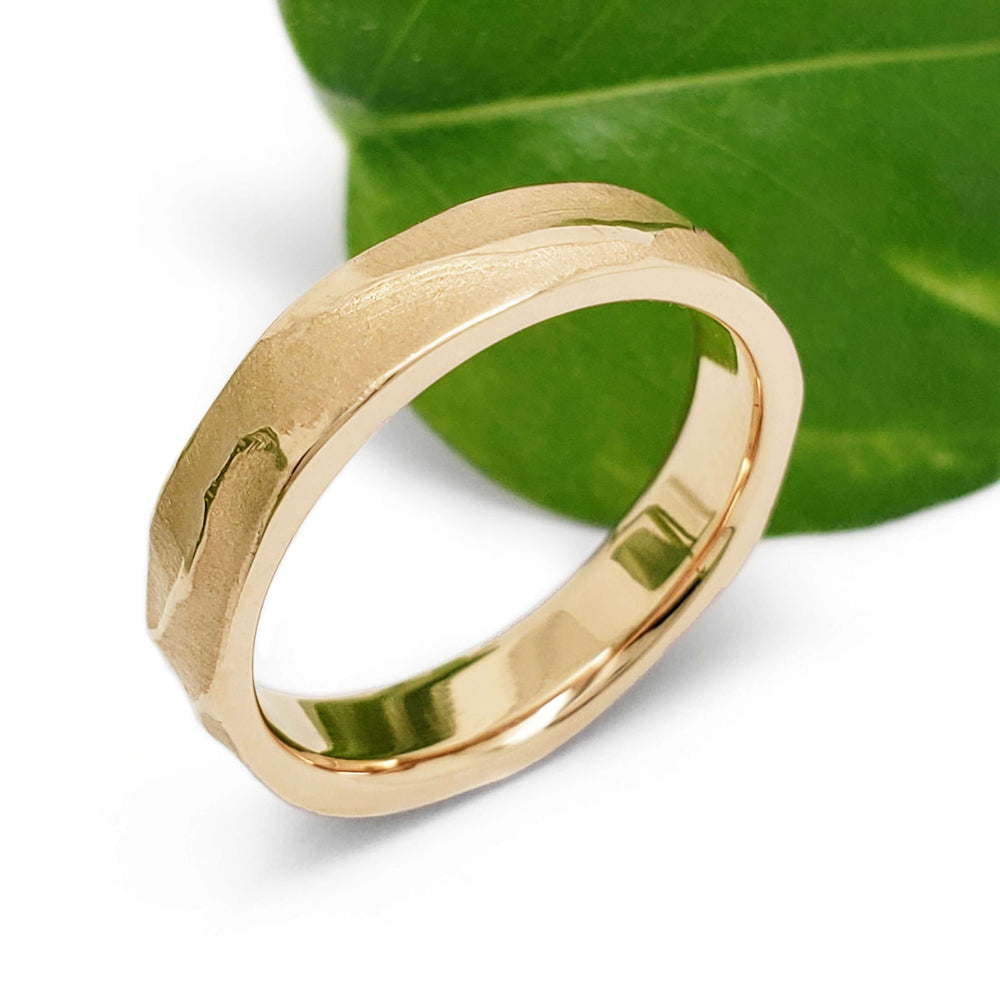 14kt yellow gold topography wedding ring beside a green leaf, side view