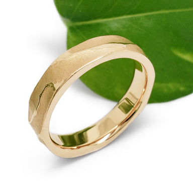 14kt yellow gold topography wedding ring beside a green leaf, side view
