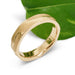 14kt yellow gold topography wedding ring beside a green leaf, side view