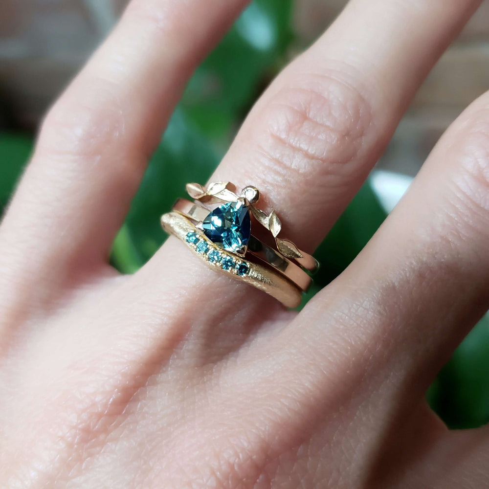 14kt yellow gold trillion sapphire ring stacked with two other gold bands on hand