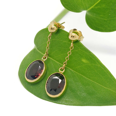Vintage 14kt yellow gold garnet dangle earrings displayed on a green leaf