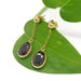 Vintage 14kt yellow gold garnet dangle earrings displayed on a green leaf