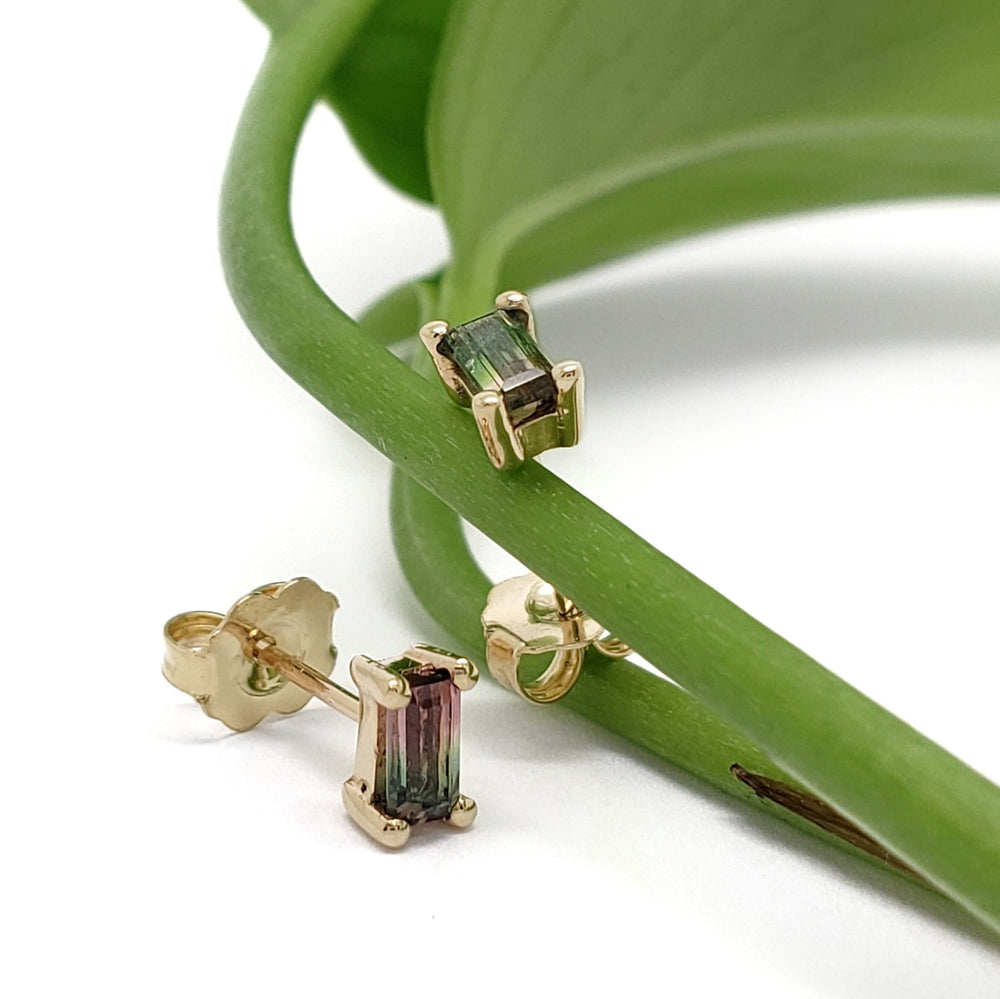 14kt yellow gold watermelon tourmaline baguette stud earrings resting on a green leaf