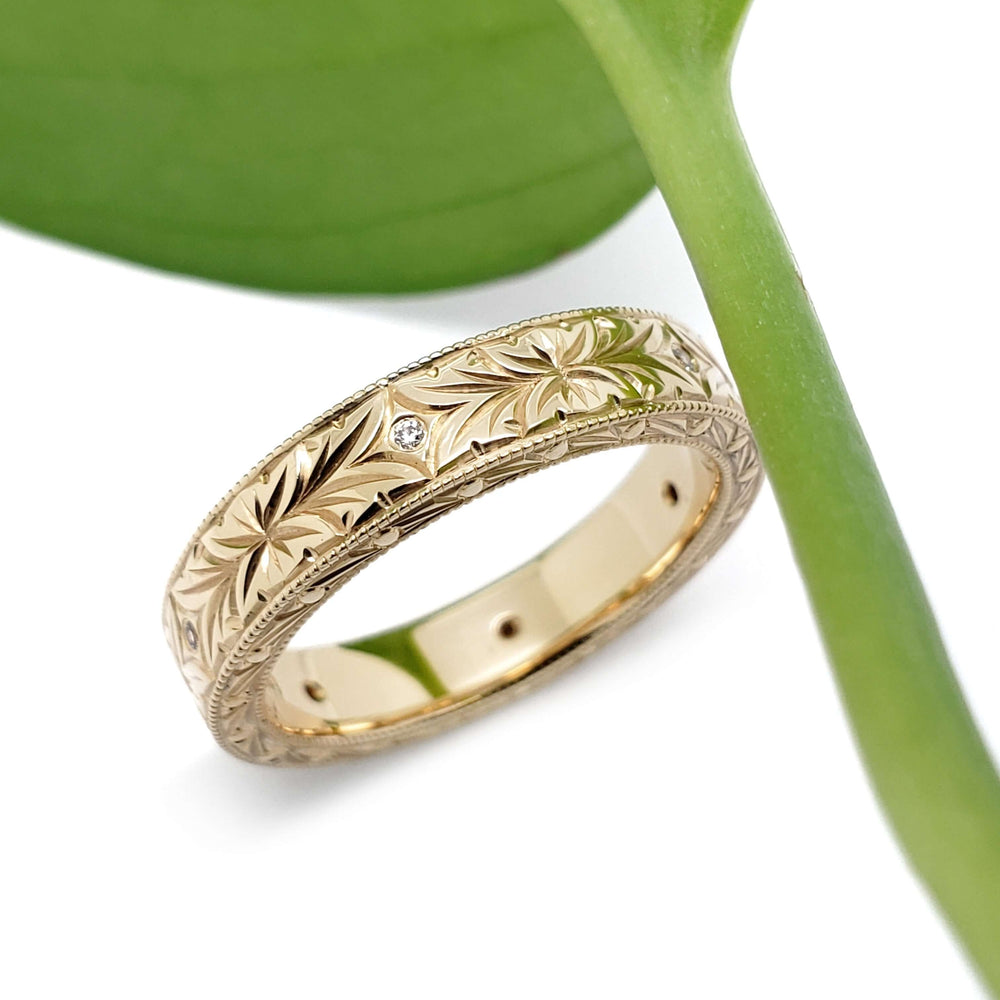 14kt yellow gold wedding band with engraved floral pattern and Canadian diamonds, near green leaf