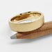 14kt yellow gold wedding band with saw blade finish resting on a pencil