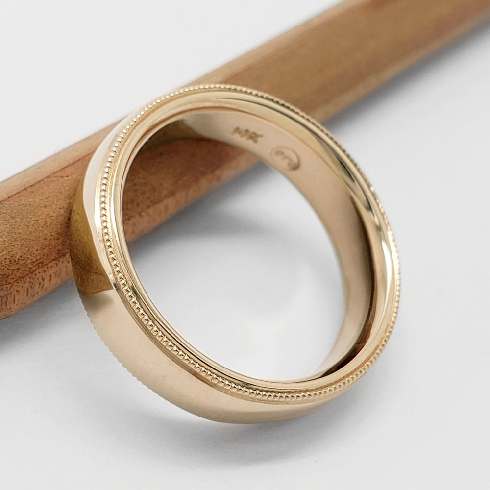 14kt yellow gold wedding ring with millgrain detail, angled view on a pencil