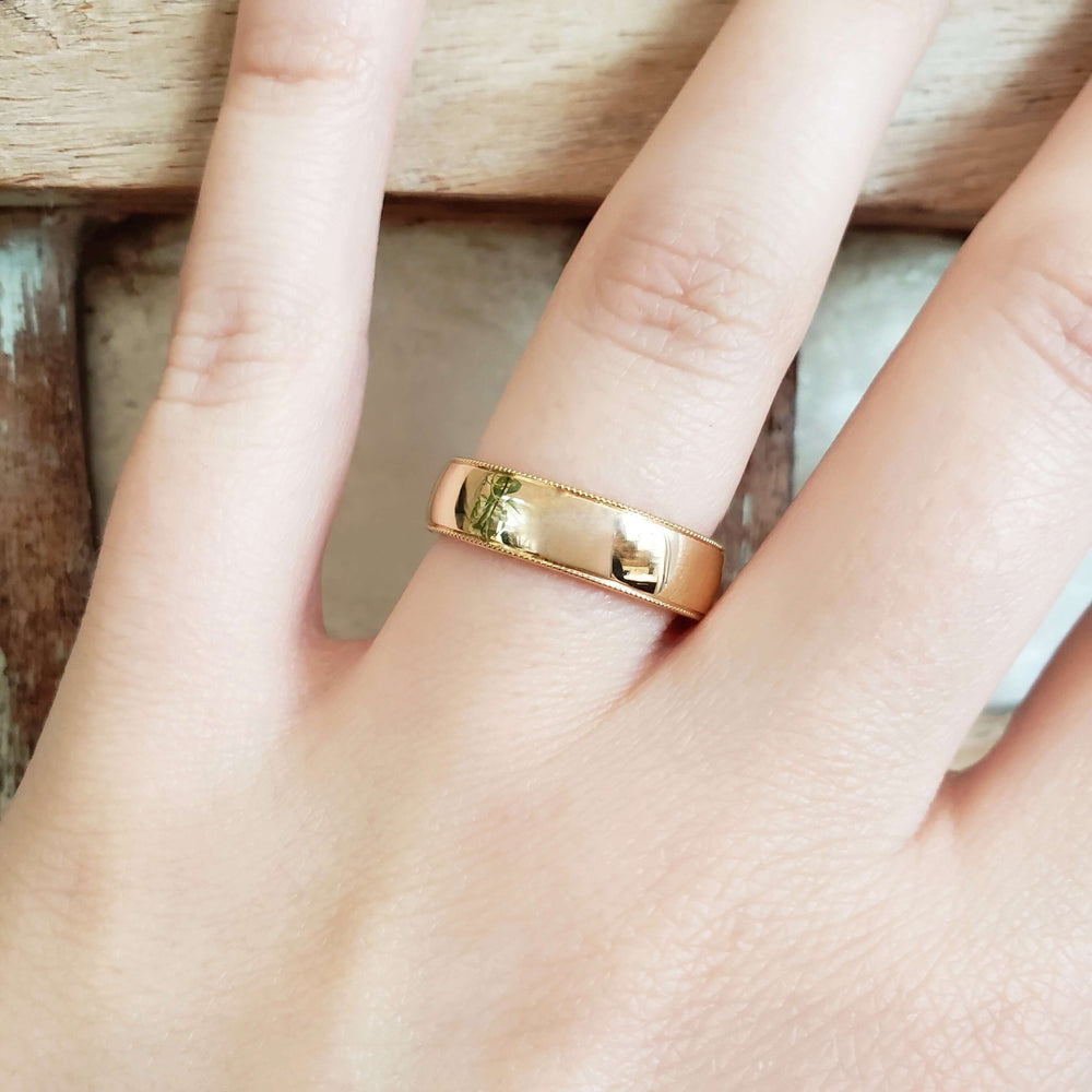 14kt yellow gold wedding ring with millgrain edge shown on a hand