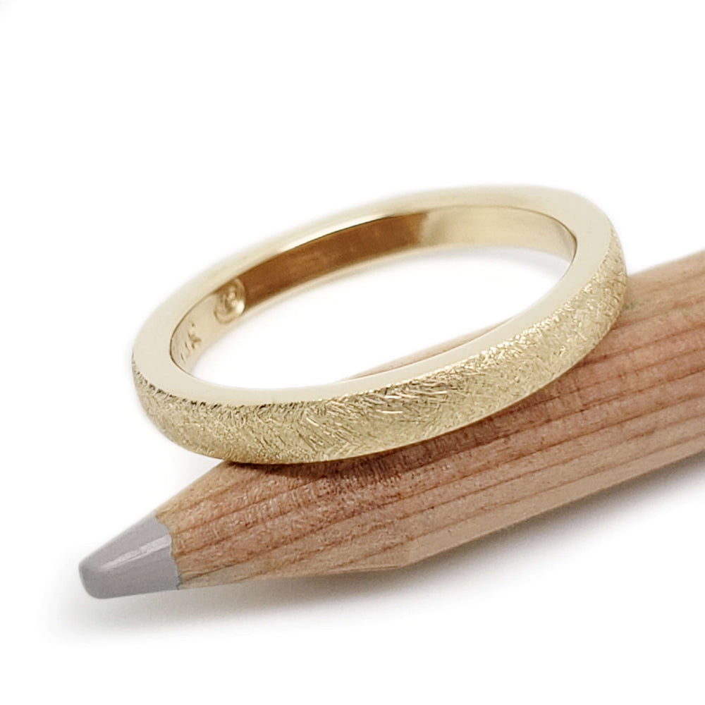 14kt yellow gold wedding ring with saw blade texture resting on a wooden pencil