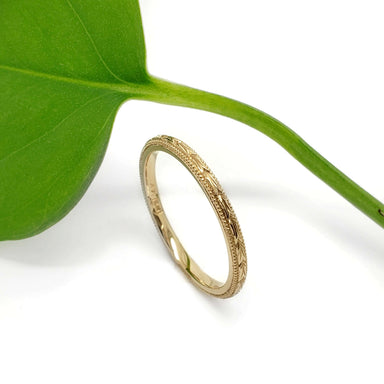 14kt yellow gold wheat engraved wedding ring displayed next to a green leaf