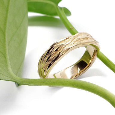 14kt yellow gold woodgrain wedding ring resting on a green leaf