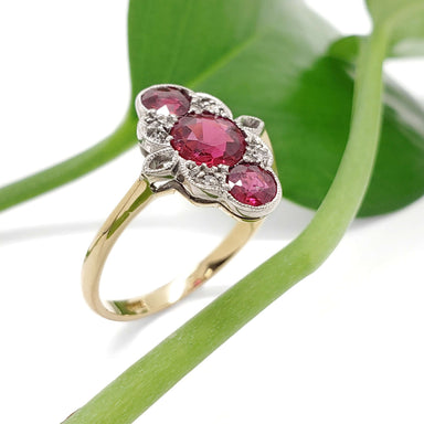 18kt gold Art Deco ring with red glass and diamond details, shown on a green leaf background