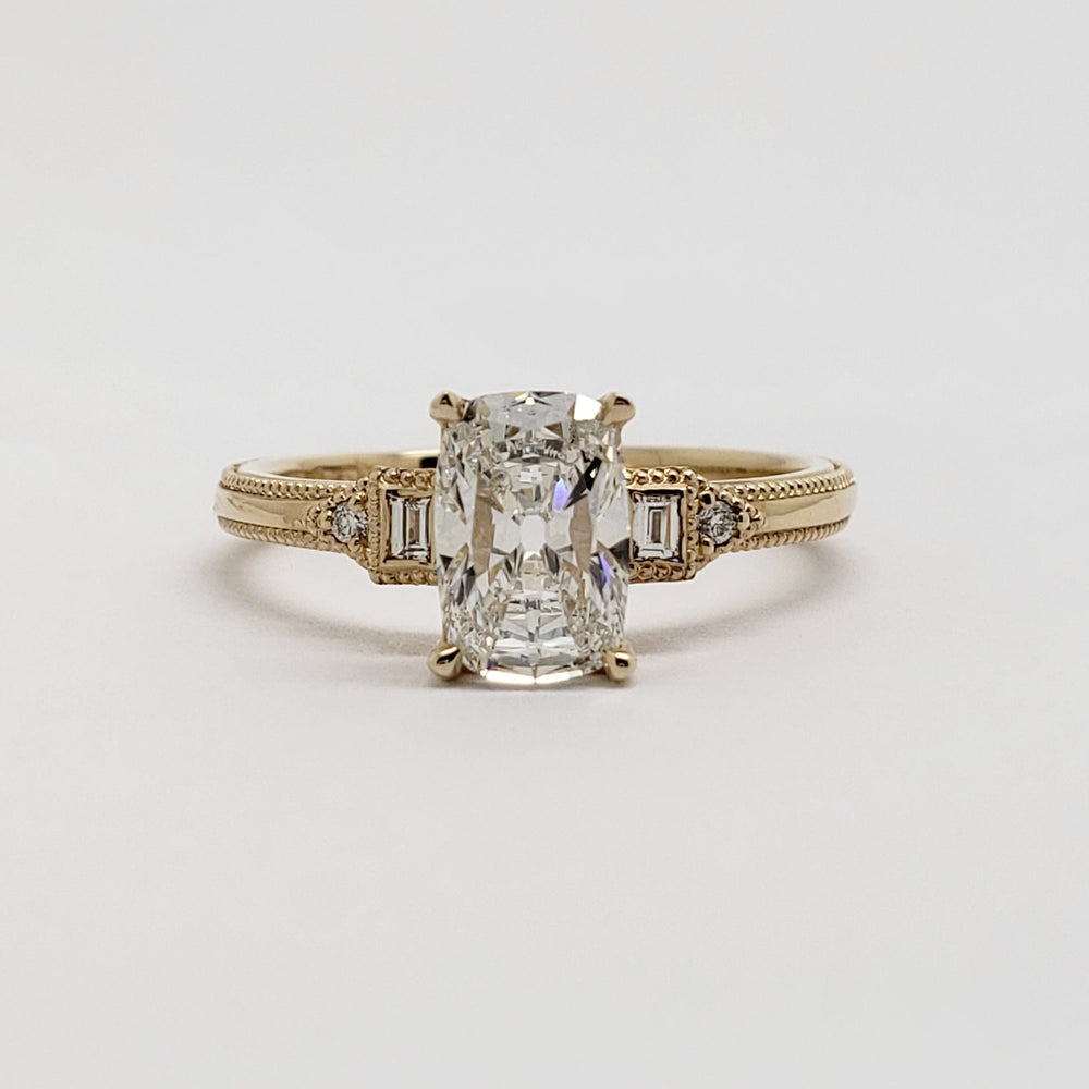 A yellow gold engagement ring featuring a large rectangular emerald-cut diamond center stone with smaller baguette and round diamonds on the shoulders, set against a clean white background.