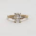 A yellow gold engagement ring featuring a large rectangular emerald-cut diamond center stone with smaller baguette and round diamonds on the shoulders, set against a clean white background.