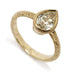 A gold ring featuring an oval-cut clear gemstone in a beaded bezel setting on an ornate, engraved band, shown on a white background.