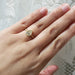 A gold ring with a marquise-cut clear gemstone worn on a person's ring finger, shown against a soft white lace background.