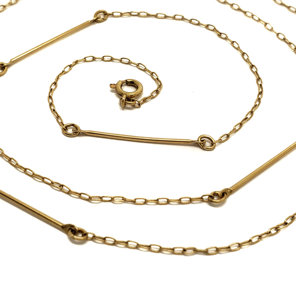 A gold chain necklace with a minimalist design, featuring alternating sections of a fine curb chain and polished bar links, coiled on a white background.
