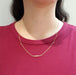 A delicate gold chain necklace with a small horizontal bar centerpiece, worn by a model wearing a magenta ribbed t-shirt.