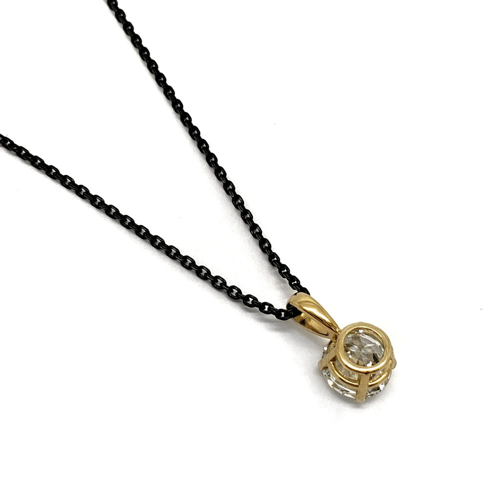 A gold pendant necklace with a clear round gemstone on a black chain, photographed on a plain white background.