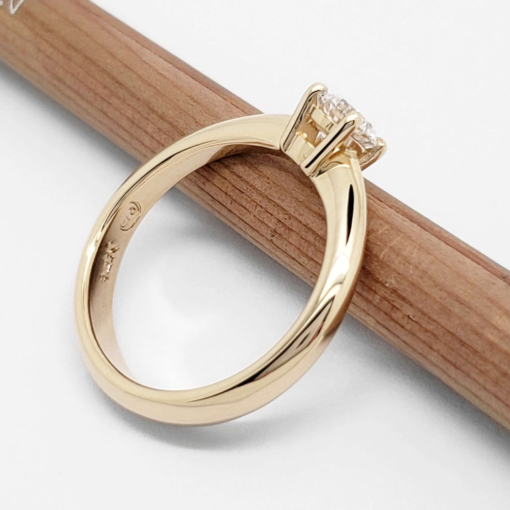 Angled side view of yellow gold solitaire ring with diamond, on wood