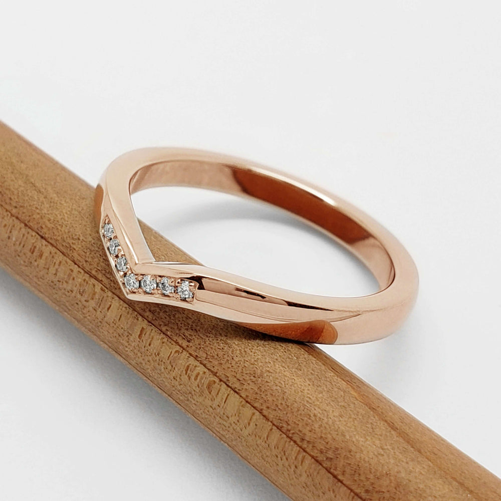 Angled view of a 14kt rose gold chevron wedding ring with diamonds on a pencil