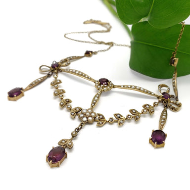 Antique amethyst and seed pearl lavaliere necklace in yellow gold beside a green leaf