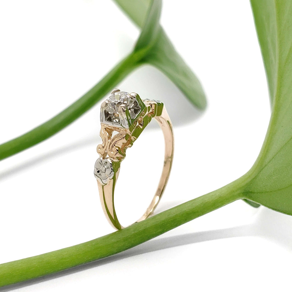 Antique diamond ring in yellow and white gold, displayed with green leaves