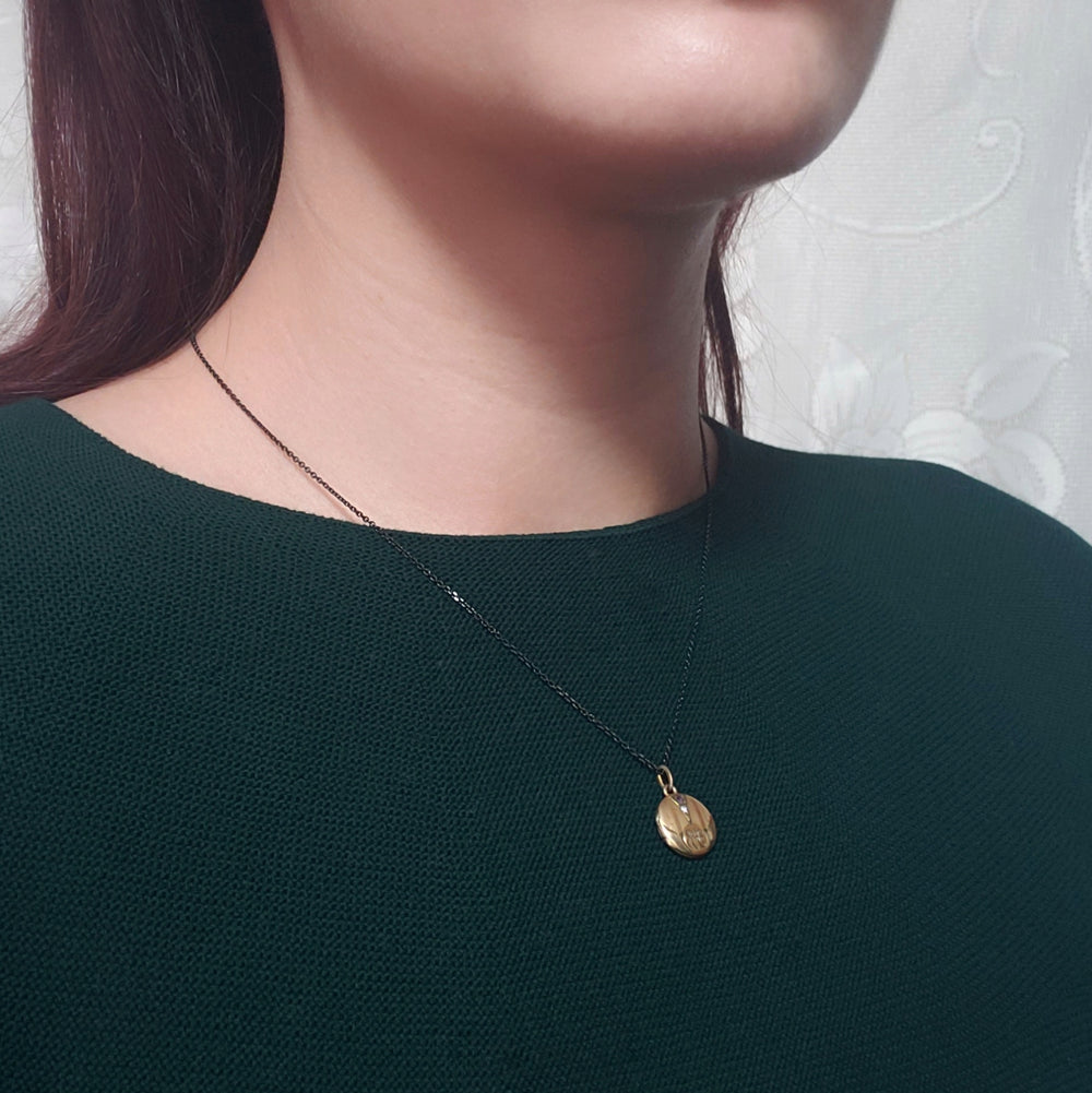 Antique gold-toned round locket on a model in a dark green top