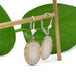 Antique oval earrings in yellow and white gold with engraved detail, hanging on a wooden rod