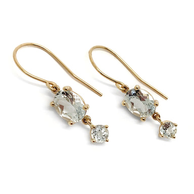 14kt yellow gold aquamarine dangle earrings displayed on a stand with green leaves