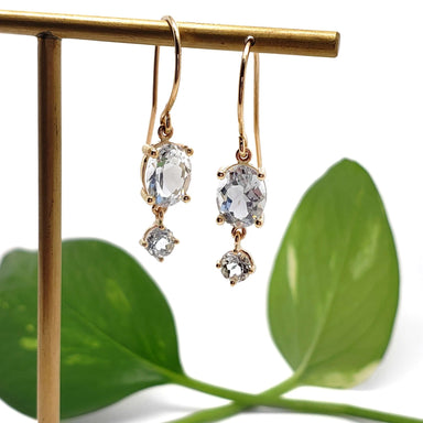 14kt yellow gold aquamarine dangle earrings displayed on a stand with green leaves