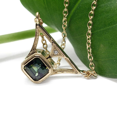 Art Deco inspired yellow gold necklace with green sapphire and diamond, on leaf background