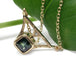 Art Deco inspired yellow gold necklace with green sapphire and diamond, on leaf background