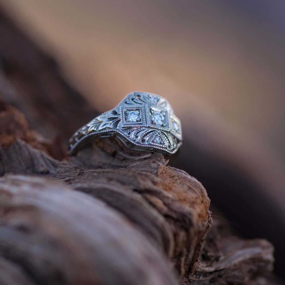 Art Deco style 19kt white gold diamond ring displayed on textured wood outdoors