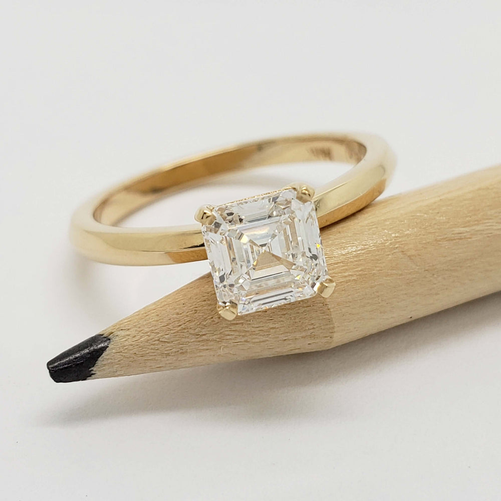 Asscher cut lab diamond engagement ring in yellow gold resting on pencil