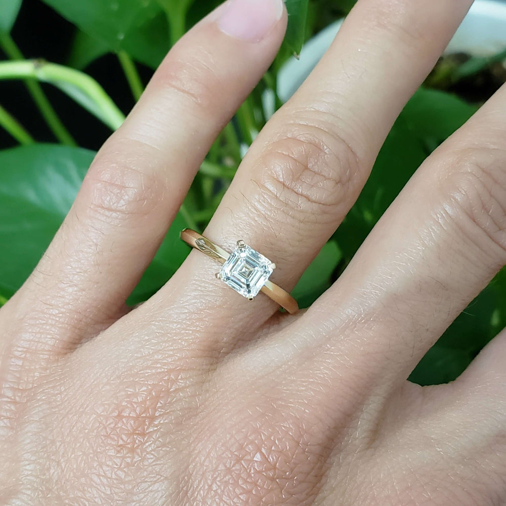 Asscher cut lab diamond yellow gold ring shown on hand with green background