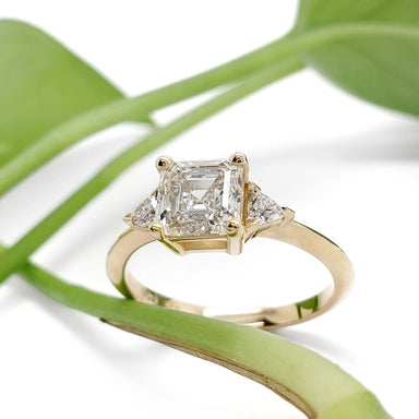 Asscher cut lab diamond engagement ring in yellow gold with side diamonds, styled with greenery