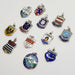 Assorted vintage silver crest and travel-themed pendants, including Gander Airport and Wiesbaden, on a white background