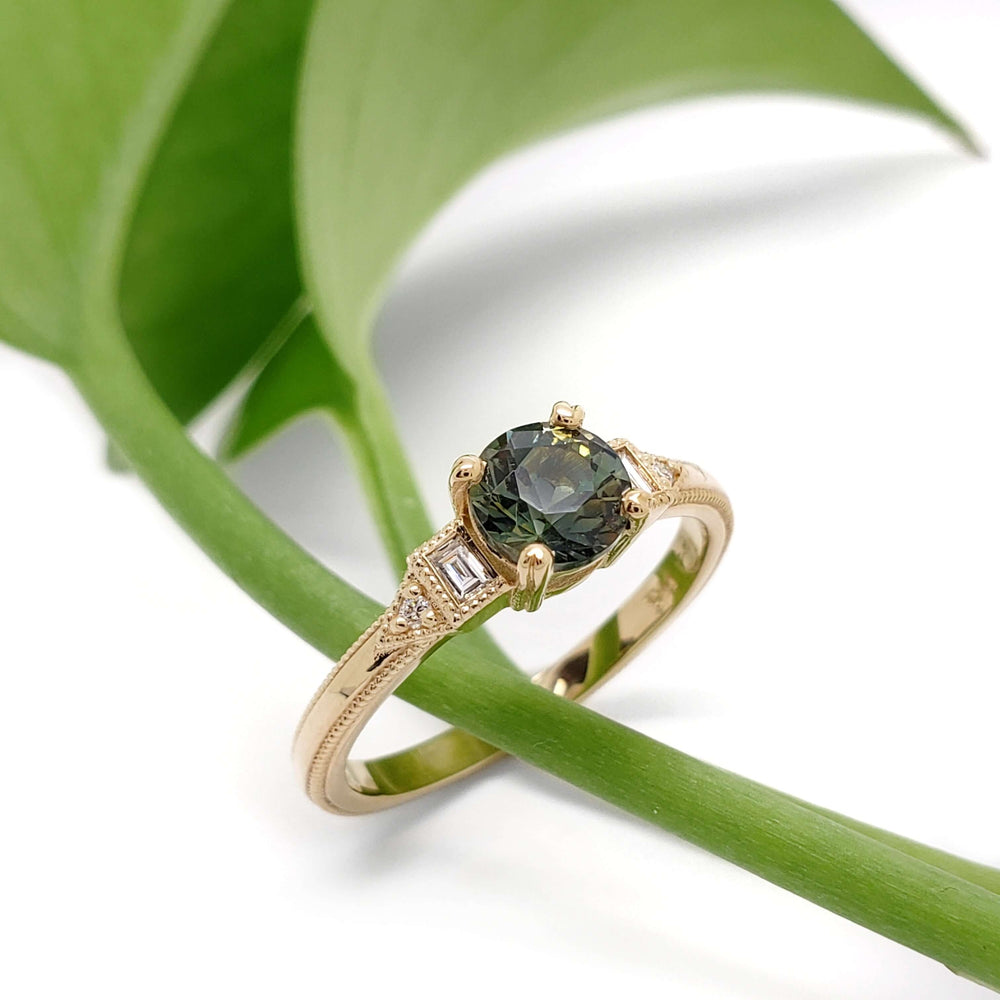 Australian sapphire and lab diamond engagement ring in yellow gold resting on a green leaf