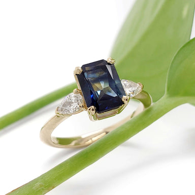 Australian sapphire and lab diamond engagement ring in yellow gold, shown with green leaves