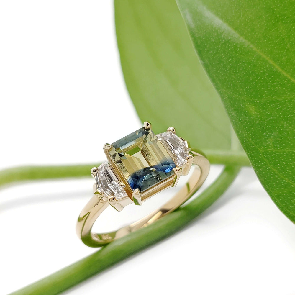 Australian sapphire and lab diamond engagement ring in yellow gold beside a green leaf