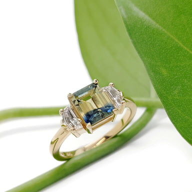 Australian sapphire and lab diamond engagement ring in yellow gold beside a green leaf