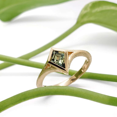 Kite-shaped Australian sapphire engagement ring in 14kt yellow gold on white background with green leaves