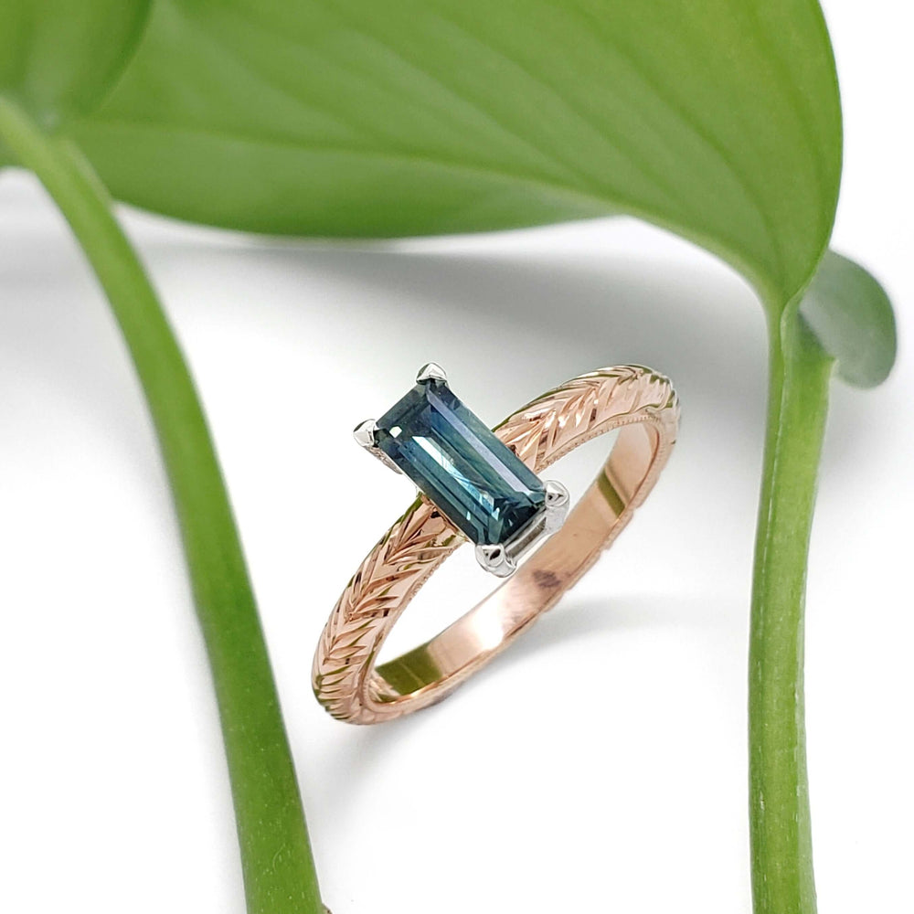 Australian sapphire engagement ring in rose gold with engraved band, shown with green leaf