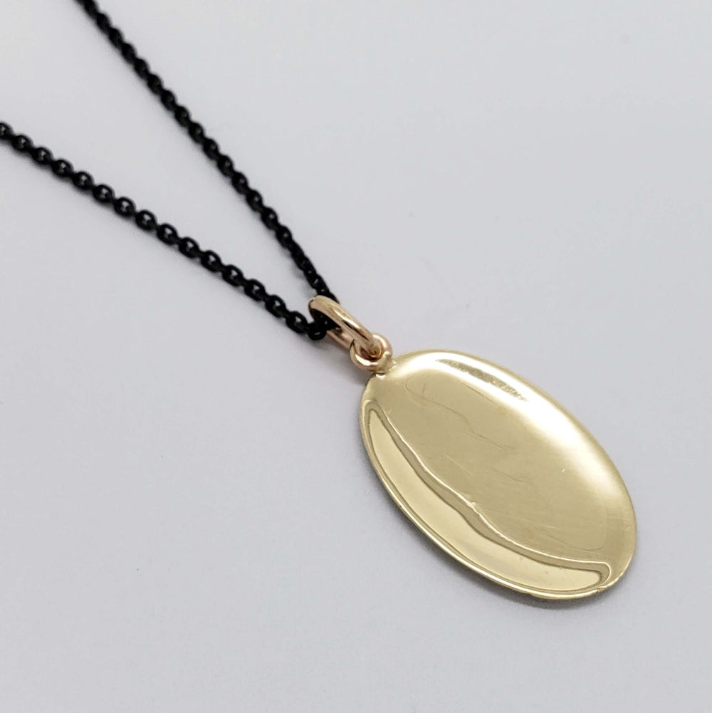 Back view of oval 14kt yellow gold pendant on a black chain